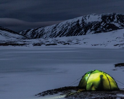 Glowing green tent in dark snowy mountains