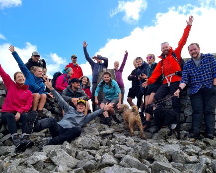 Group of 16 and brown dog raising their hands in the air