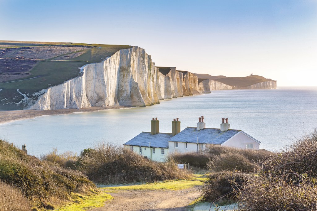 The coastguard cottages, Eastbourne. White chalk cliffs, two small white buildings with grey stone rooves and a panoramic sea view