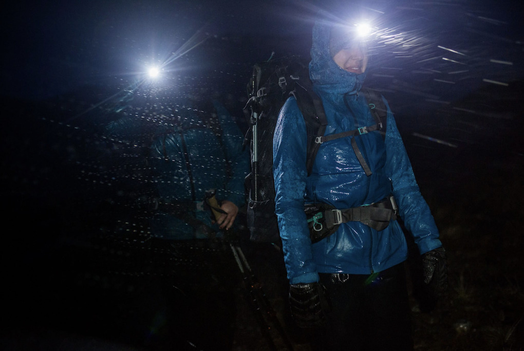 Two walkers in blue coats walking in pitch black and rain with bright head torches on