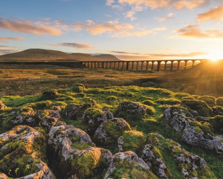 Golden sun over tall bridge arches with three peaks beyond