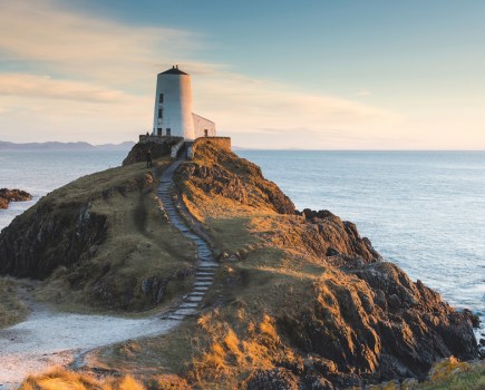 Lighthouse Ynys Llanddwyn on a mound above the sea with a grey stone staircase and rocky coastal terain